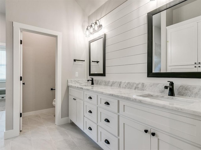 full bath featuring toilet, double vanity, baseboards, and a sink