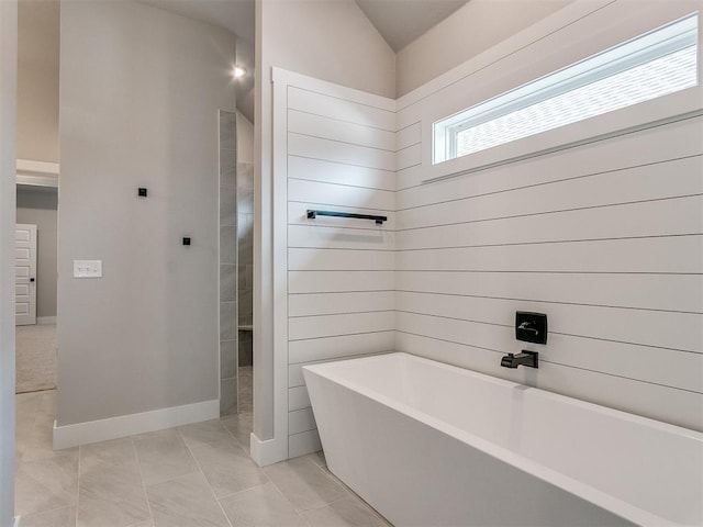 bathroom with vaulted ceiling, a soaking tub, tile patterned flooring, and baseboards