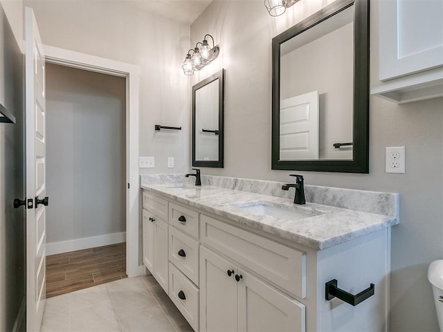 bathroom with toilet, a sink, baseboards, and double vanity