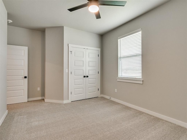 unfurnished bedroom featuring a ceiling fan, baseboards, a closet, and light colored carpet