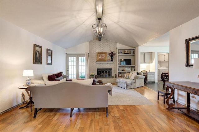 living room with lofted ceiling, built in shelves, a fireplace, a chandelier, and light wood-type flooring