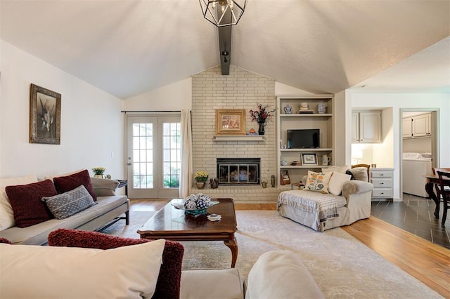 living room with hardwood / wood-style floors, washing machine and clothes dryer, a brick fireplace, a notable chandelier, and vaulted ceiling with beams