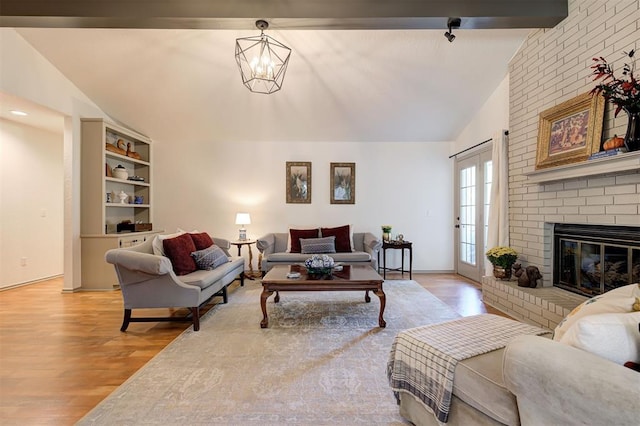 living room featuring light wood-type flooring, an inviting chandelier, a fireplace, and vaulted ceiling with beams