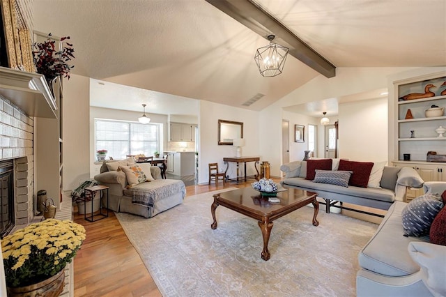 living room with lofted ceiling with beams, a fireplace, an inviting chandelier, and light hardwood / wood-style floors