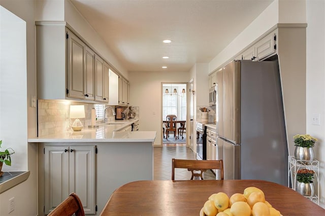 kitchen featuring light tile patterned floors, kitchen peninsula, stainless steel appliances, tasteful backsplash, and sink