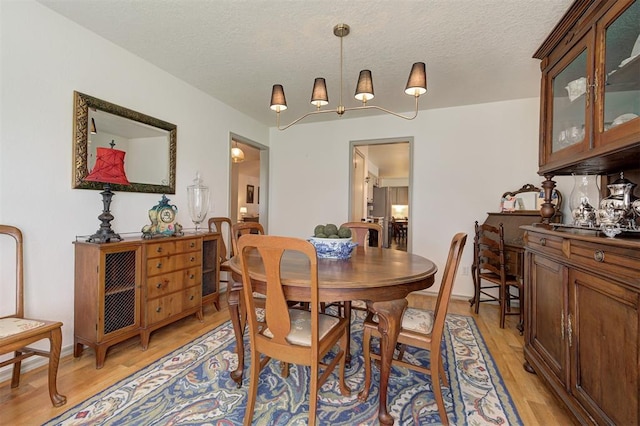 dining area featuring a textured ceiling, light hardwood / wood-style flooring, and an inviting chandelier