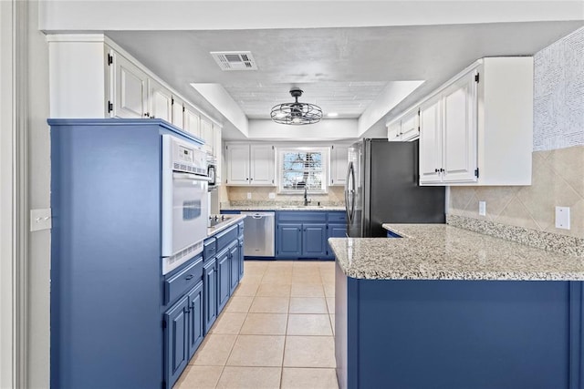 kitchen featuring appliances with stainless steel finishes, white cabinets, blue cabinets, a raised ceiling, and kitchen peninsula