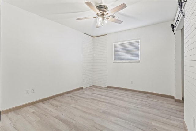 unfurnished room with light hardwood / wood-style floors, ceiling fan, and a barn door