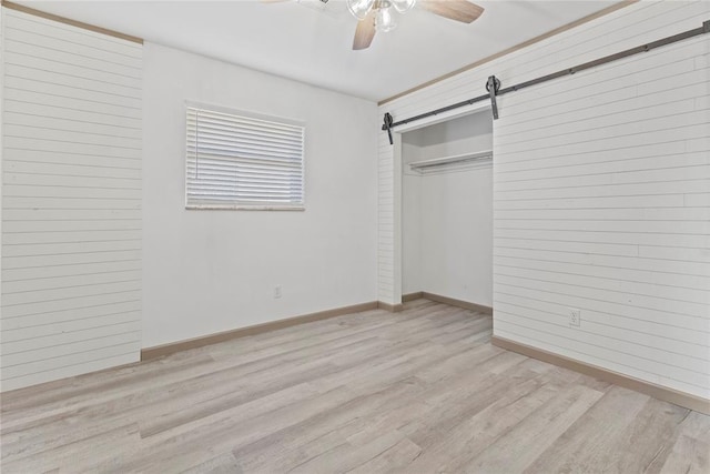 unfurnished bedroom with light wood-type flooring, a closet, ceiling fan, and a barn door