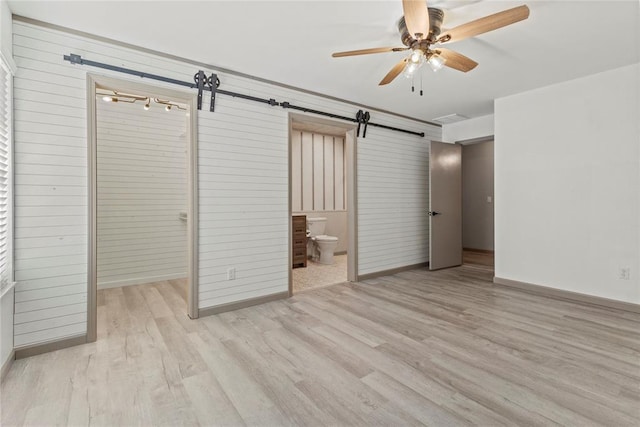 unfurnished bedroom with ceiling fan, a barn door, connected bathroom, light hardwood / wood-style floors, and a closet