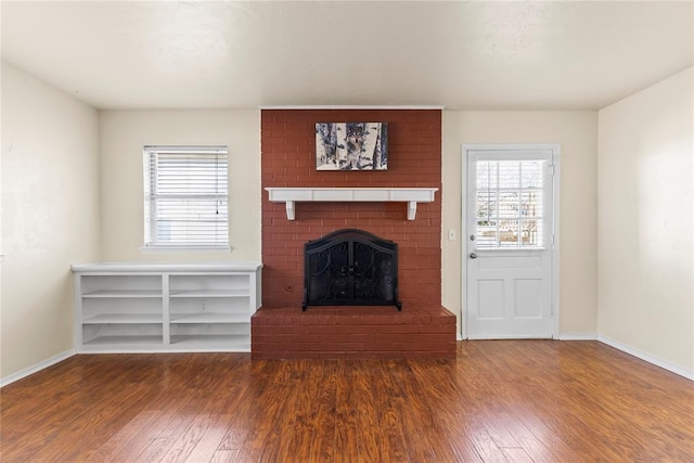 unfurnished living room featuring dark wood-type flooring and a brick fireplace