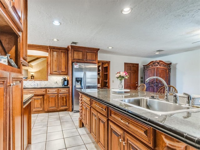 kitchen featuring a textured ceiling, sink, backsplash, stainless steel fridge with ice dispenser, and light tile patterned flooring