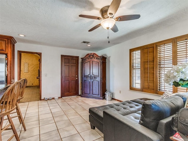 living room with ceiling fan, a textured ceiling, and light tile patterned flooring