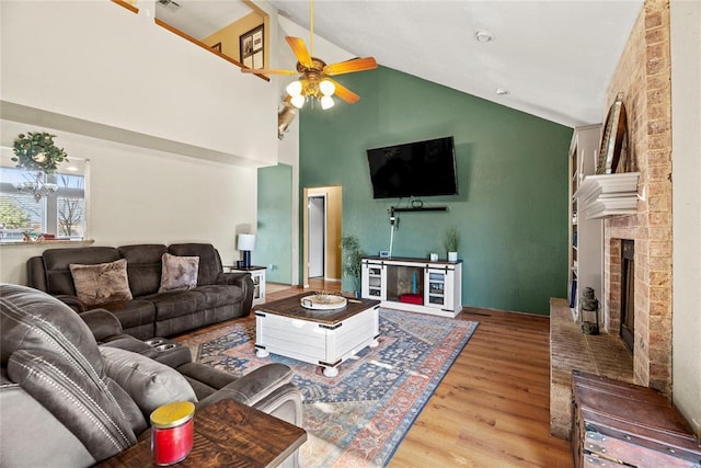 living room featuring ceiling fan, a fireplace, high vaulted ceiling, and wood-type flooring