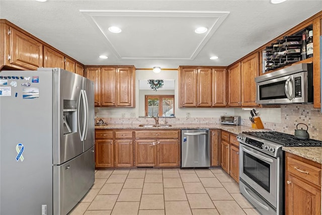 kitchen with light tile patterned flooring, sink, light stone counters, tasteful backsplash, and appliances with stainless steel finishes