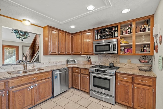 kitchen with sink, appliances with stainless steel finishes, tasteful backsplash, light stone countertops, and light tile patterned flooring