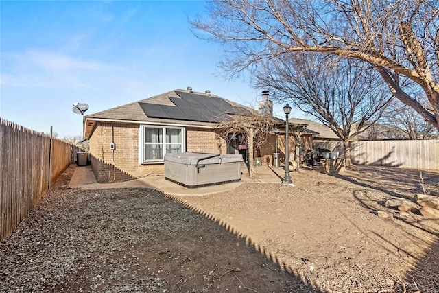 rear view of property with central AC unit, a patio area, a hot tub, and solar panels