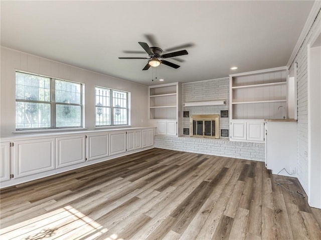 unfurnished living room with light wood-type flooring, a brick fireplace, built in features, and ceiling fan