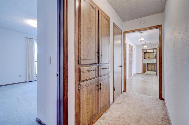 hall with light colored carpet and a textured ceiling