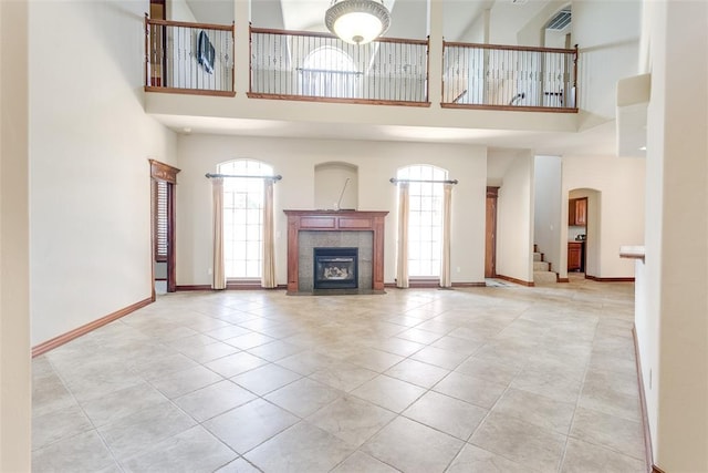 unfurnished living room featuring light tile patterned flooring, a towering ceiling, plenty of natural light, and a tile fireplace