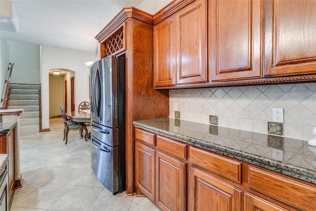 kitchen with light tile patterned flooring, backsplash, stainless steel fridge, and dark stone counters