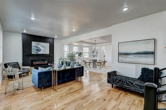 living room with a tray ceiling, light hardwood / wood-style flooring, a chandelier, and a fireplace