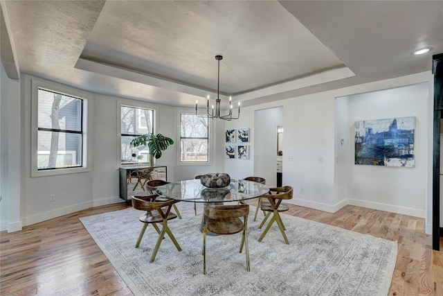 dining room with a tray ceiling, an inviting chandelier, and light wood-type flooring