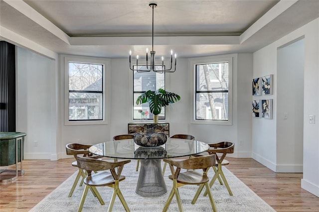 dining space with light hardwood / wood-style flooring, a raised ceiling, and a notable chandelier