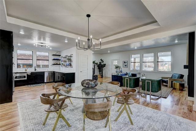 dining room with a raised ceiling, a healthy amount of sunlight, and light wood-type flooring