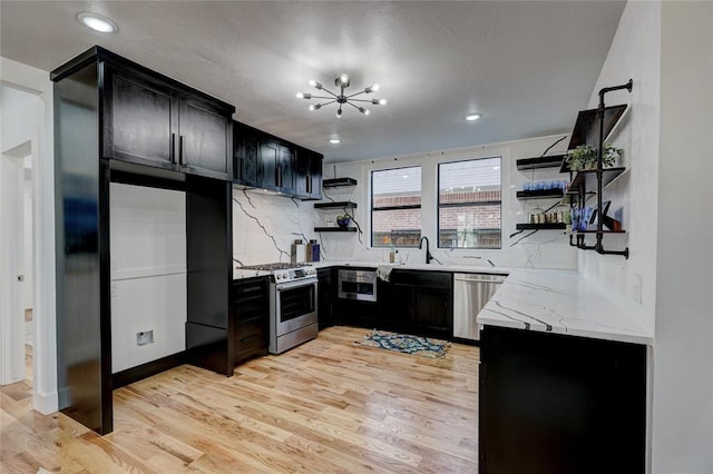 kitchen with light stone countertops, appliances with stainless steel finishes, light hardwood / wood-style floors, backsplash, and a chandelier