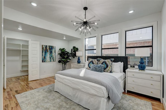 bedroom with a spacious closet, a closet, a chandelier, and light wood-type flooring