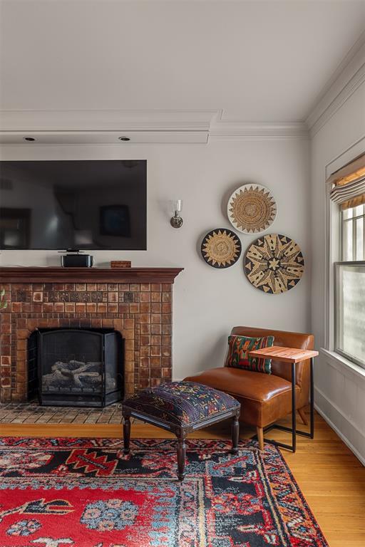 living area with a brick fireplace, wood-type flooring, and ornamental molding