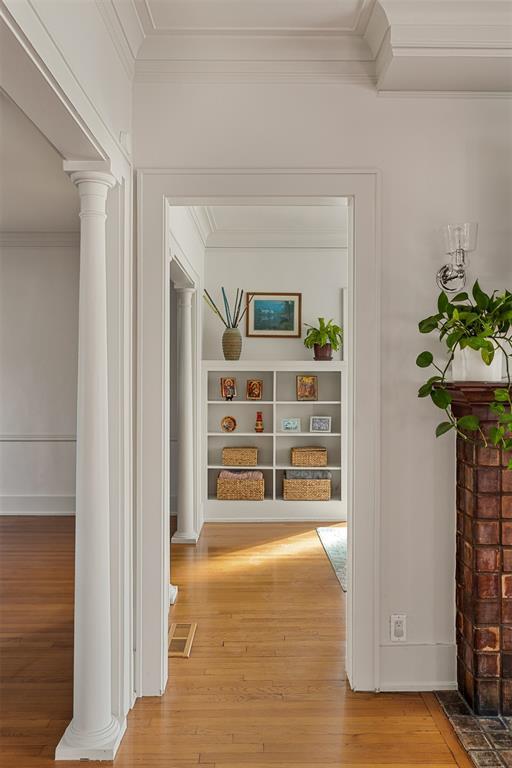 corridor with crown molding, built in shelves, hardwood / wood-style flooring, and ornate columns