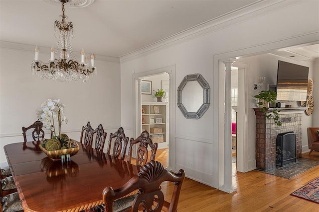 dining room with ornate columns, a chandelier, hardwood / wood-style flooring, crown molding, and a brick fireplace