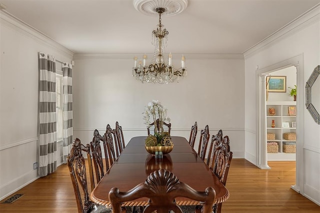 dining space with ornamental molding, wood-type flooring, and a notable chandelier