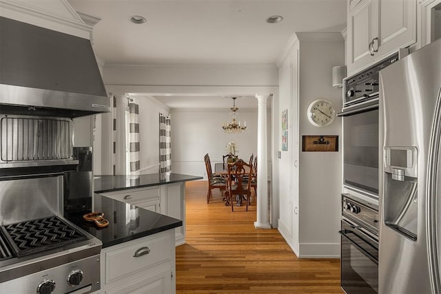 kitchen featuring ornate columns, appliances with stainless steel finishes, hardwood / wood-style floors, ventilation hood, and white cabinetry