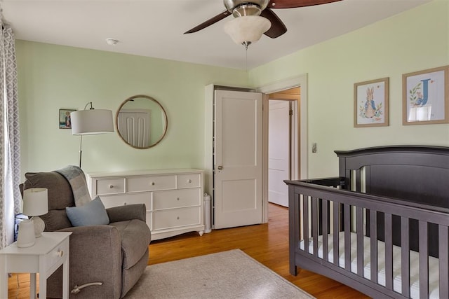 bedroom with a nursery area, ceiling fan, and light wood-type flooring