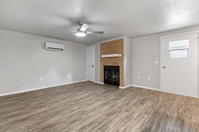 unfurnished living room with an AC wall unit, hardwood / wood-style floors, a textured ceiling, a fireplace, and ceiling fan