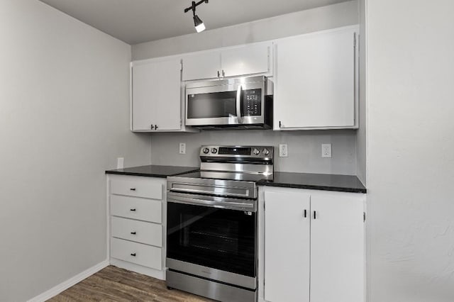 kitchen with dark wood-type flooring, white cabinets, appliances with stainless steel finishes, and track lighting