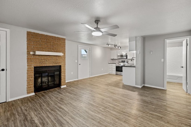 unfurnished living room featuring ceiling fan, a fireplace, sink, light hardwood / wood-style flooring, and a textured ceiling