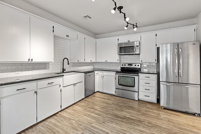 kitchen with appliances with stainless steel finishes, white cabinetry, light hardwood / wood-style floors, sink, and backsplash