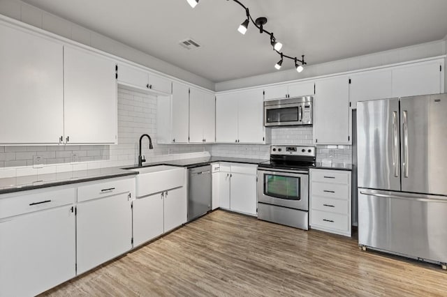 kitchen with light hardwood / wood-style floors, decorative backsplash, sink, white cabinetry, and stainless steel appliances