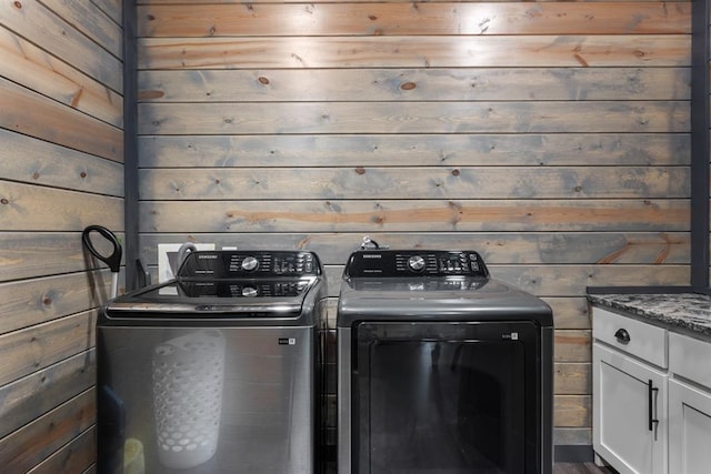 laundry room featuring wooden walls, cabinets, and separate washer and dryer