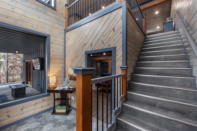 stairway with wood ceiling, a high ceiling, and wooden walls