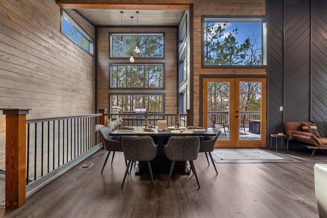 dining space featuring french doors, plenty of natural light, a high ceiling, and wooden walls