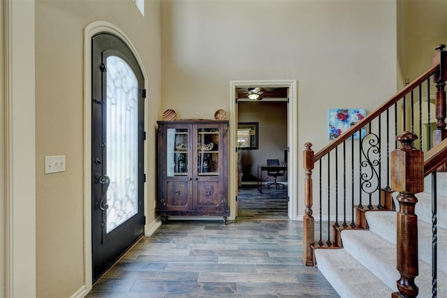 entrance foyer with wood finished floors, stairway, arched walkways, a high ceiling, and baseboards