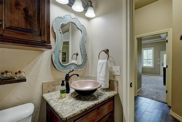 bathroom featuring toilet, wood finished floors, baseboards, vanity, and a textured wall