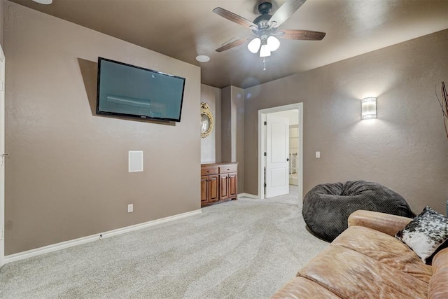 living room featuring a ceiling fan, light colored carpet, baseboards, and a textured wall