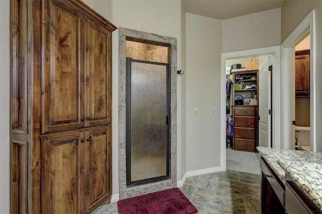 bathroom featuring a walk in closet, baseboards, vanity, and a shower stall