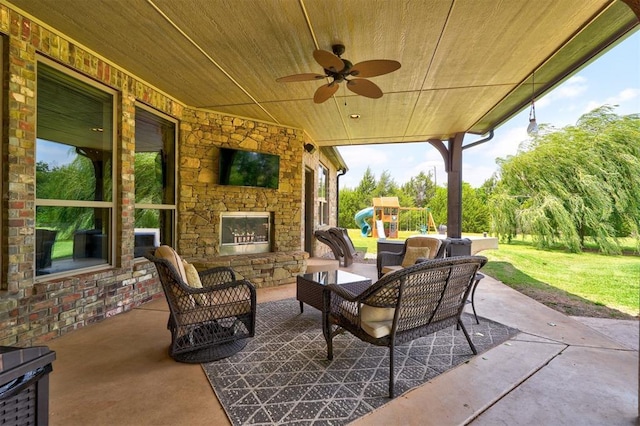 view of patio / terrace with an outdoor living space with a fireplace, a playground, and ceiling fan